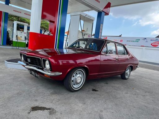 Classic burgundy car parked at a gas station under a blue sky.